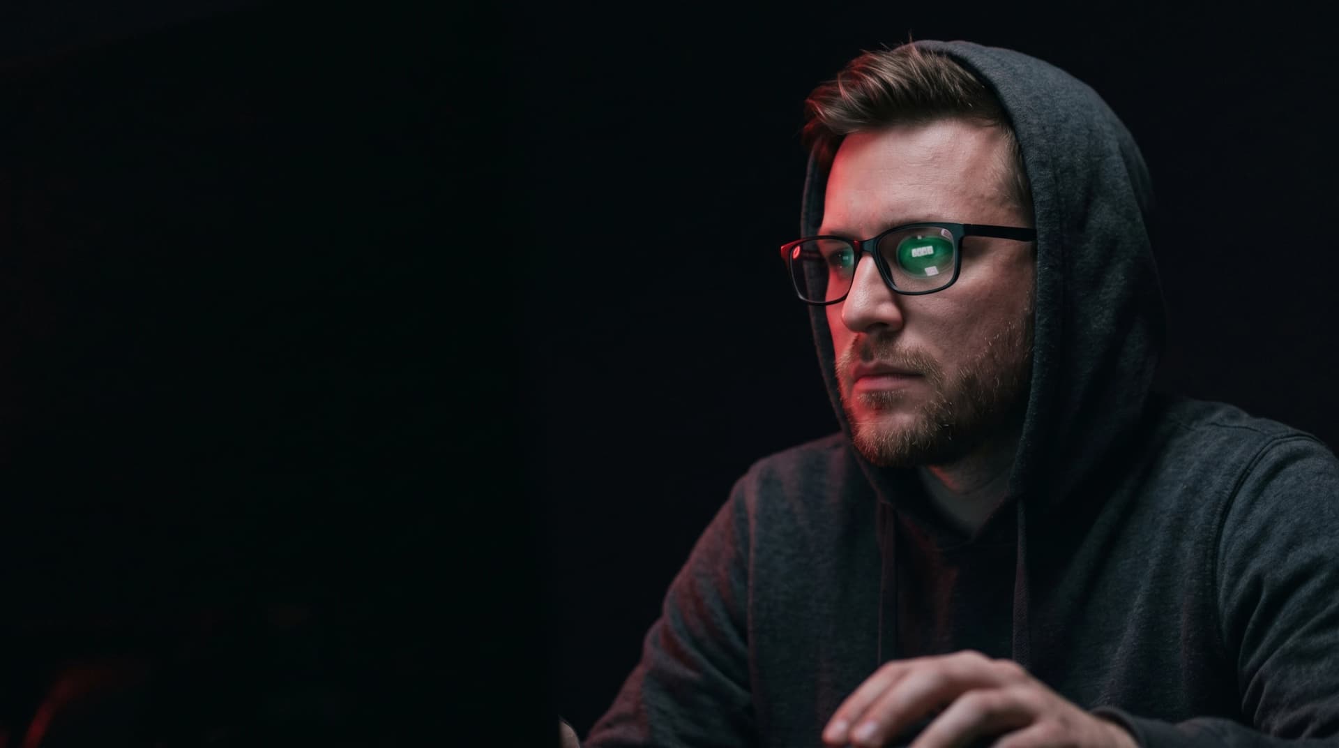 Joueur de poker online encapuchonné dans la pénombre, lunettes reflétant une table de poker en ligne