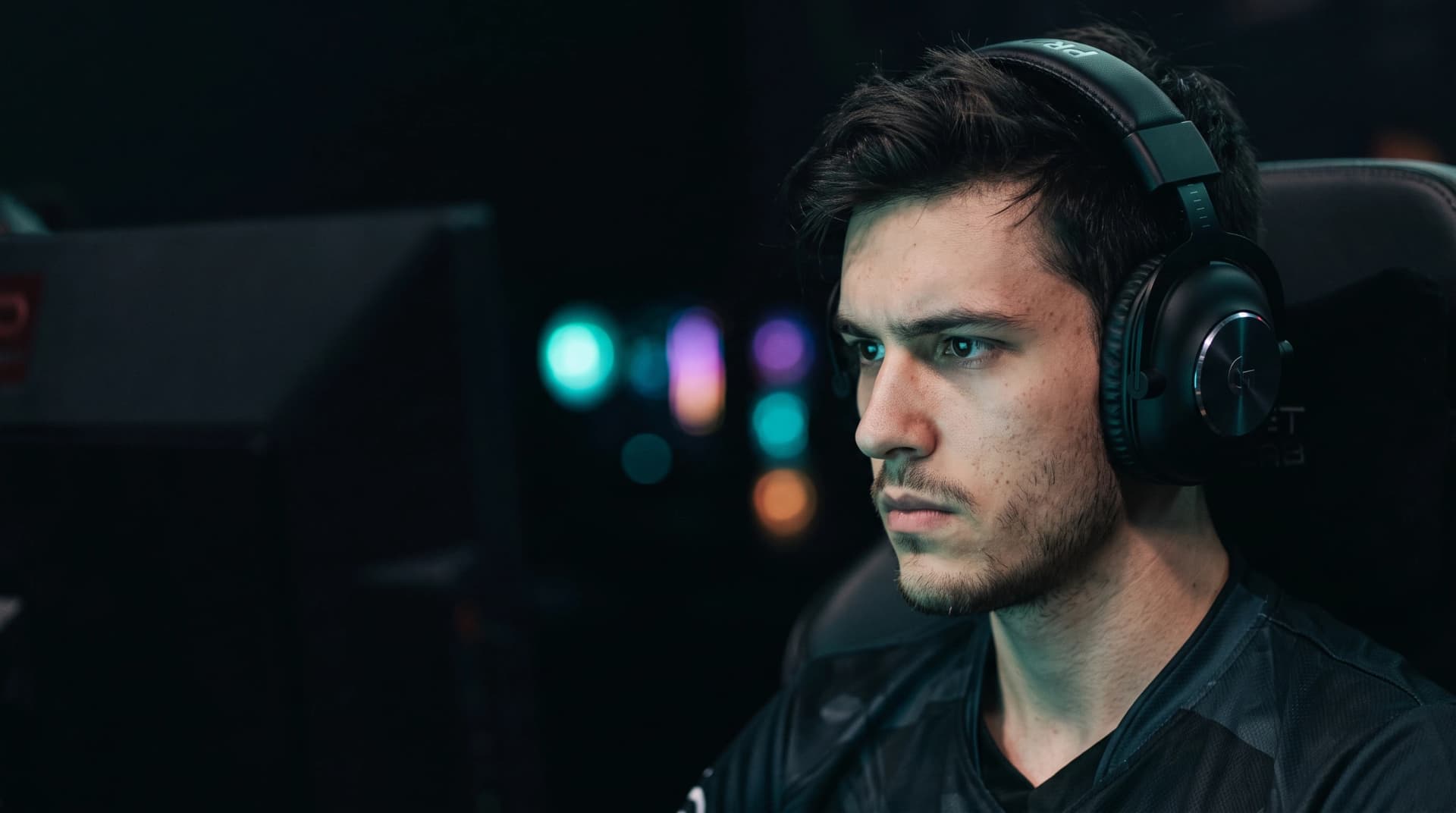Joueur d'esport casque sur les oreilles, concentré face à son écran dans une salle sombre